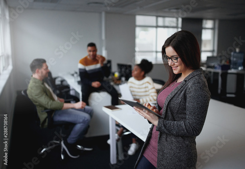 American Businesswoman using digital tablet by desk with colleagues discussing in background at office startup entrepreneur 