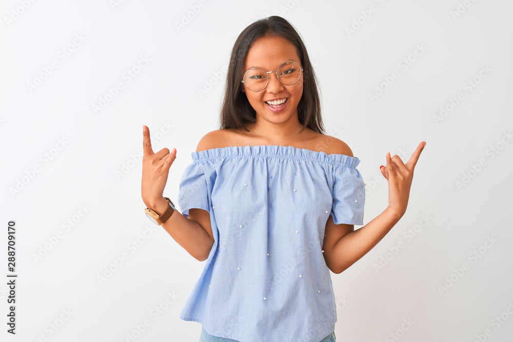 Young chinese woman wearing blue t-shirt and glasses over isolated white background shouting with crazy expression doing rock symbol with hands up. Music star. Heavy concept. Young chinese woman wearing blue t-shirt and glasses over isolated white background shouting with crazy expression doing rock symbol with hands up. Music star. Heavy concept.