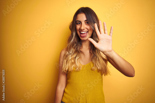Young beautiful woman wearing t-shirt over yellow isolated background showing and pointing up with fingers number five while smiling confident and happy.
