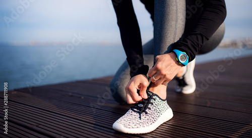 A young sportswoman with smartwatch outdoors on beach, tying shoelaces.
