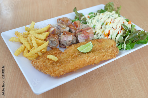 Fried fish, bacon roll, french fries, vegetable salad in white plate