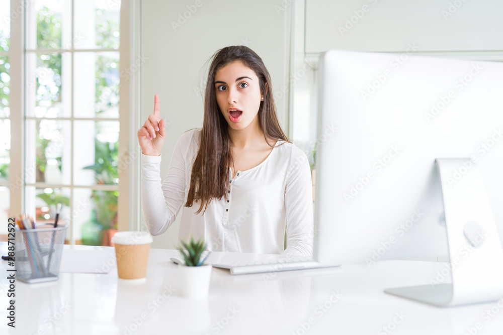 Beautiful young woman working using computer pointing finger up with successful idea. Exited and happy. Number one. Beautiful young woman working using computer pointing finger up with successful idea. Exited and happy. Number one.