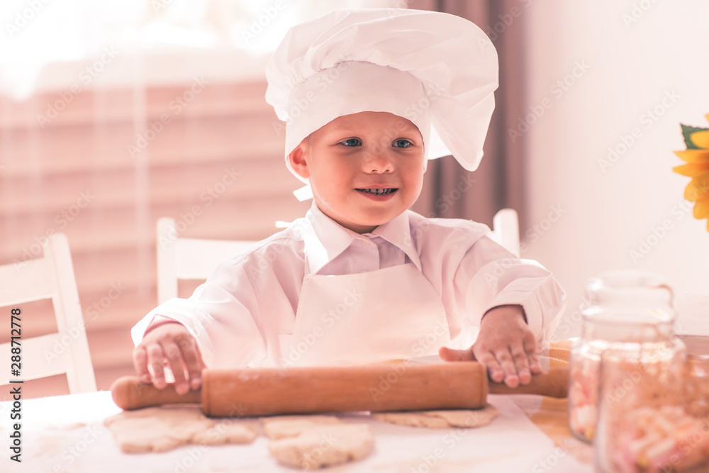 little baby in a cook rolls out the dough with rolling pin and smiling little baby in a cook rolls out the dough with rolling pin and smiling