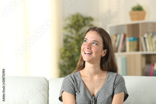 Happy woman dreaming looking at side sitting at home