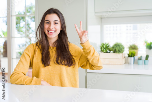 Beautiful young woman wearing yellow sweater showing and pointing up with fingers number two while smiling confident and happy.