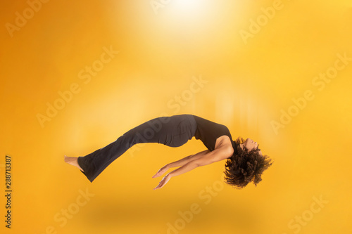 Side view of afro hair woman in zero gravity or being abducted by a UFO. Girl is flying or floating in the air. Side view of person. Over yellow background. Spiritism. Rising to the heaven. photo