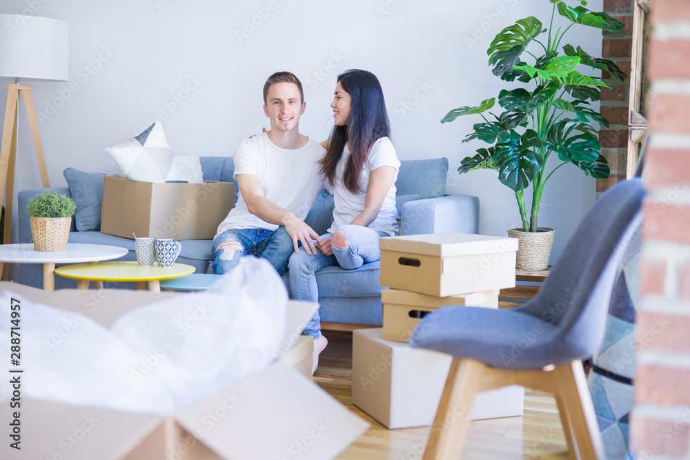 Young beautiful couple sitting on the sofa drinking coffee at new home around cardboard boxes