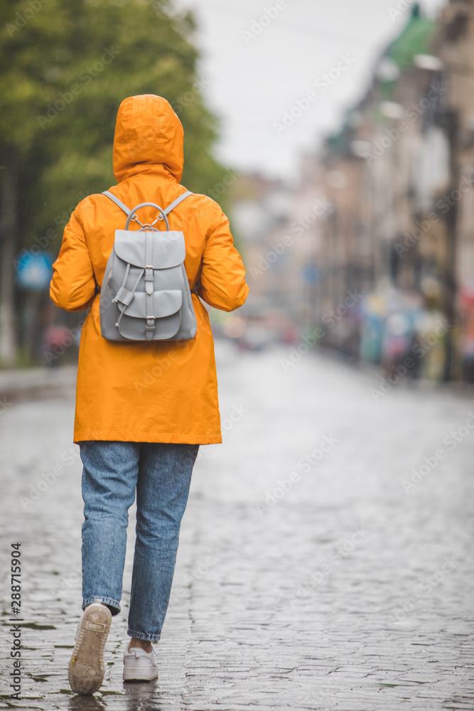woman in yellow raincoat walking by city streets under rain - obrazy, fototapety, plakaty 