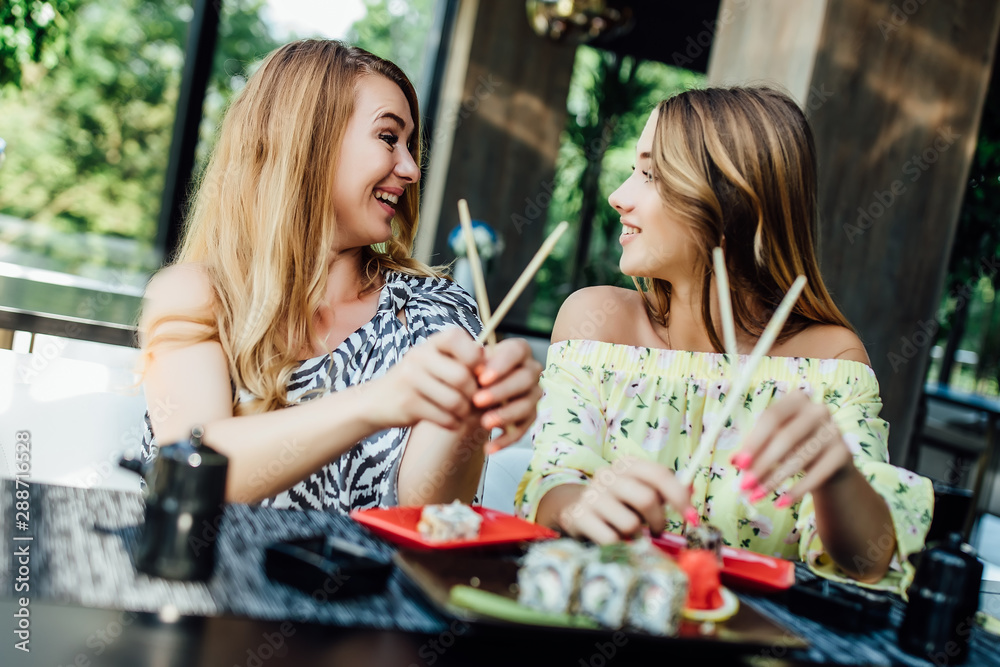 Fototapeta premium Young beautiful mother eating sushi rolls in modern cafe terrace one summer day. Family concept.