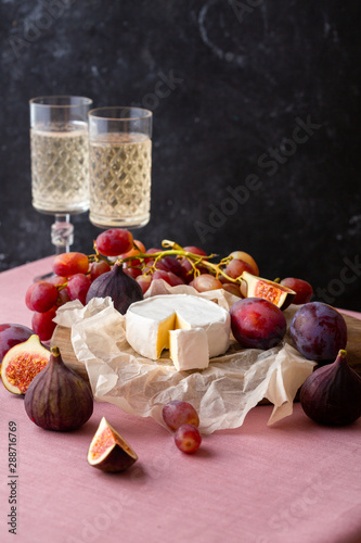 brie cheese on parchment paper with figs, plums and grape and champagne on background