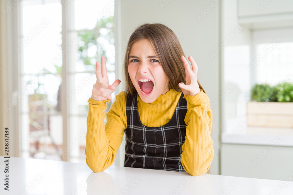 Young beautiful blonde kid girl wearing casual yellow sweater at home crazy and mad shouting and yelling with aggressive expression and arms raised. Frustration concept. Young beautiful blonde kid girl wearing casual yellow sweater at home crazy and mad shouting and yelling with aggressive expression and arms raised. Frustration concept.