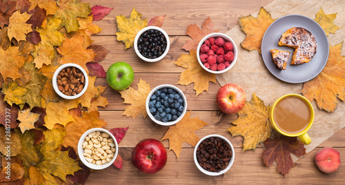 Fototapeta Naklejka Na Ścianę i Meble -  Seasonal autumn background. Frame of maple leaves and a cake, berries, raisins, apples, fruits, coffee and nuts over wooden background.