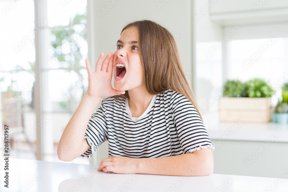 Beautiful young girl kid wearing stripes t-shirt shouting and screaming loud to side with hand on mouth. Communication concept. Beautiful young girl kid wearing stripes t-shirt shouting and screaming loud to side with hand on mouth. Communication concept.