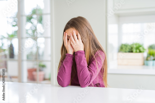 Beautiful young girl kid on white table with sad expression covering face with hands while crying. Depression concept.