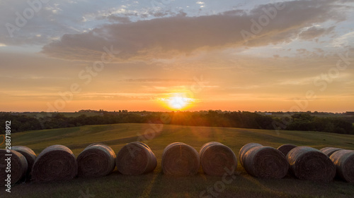 Sunrise over rows of round hay bales in a rural countryside field