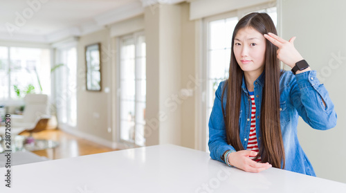 Foto Young beautiful asian woman with long hair wearing denim jacket Shooting and killing oneself pointing hand and fingers to head like gun, suicide gesture