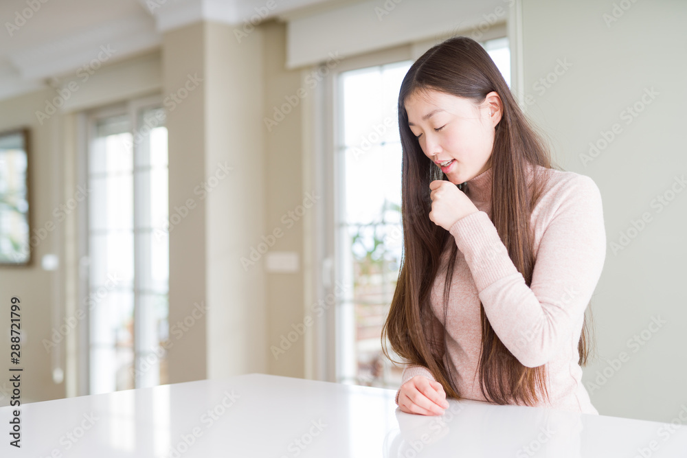 Beautiful Asian woman wearing casual sweater on white table feeling unwell and coughing as symptom for cold or bronchitis. Healthcare concept. Beautiful Asian woman wearing casual sweater on white table feeling unwell and coughing as symptom for cold or bronchitis. Healthcare concept.