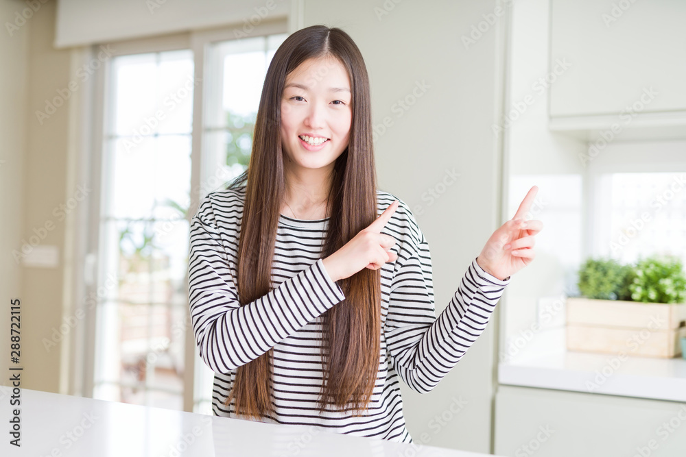 Beautiful Asian woman wearing stripes sweater smiling and looking at the camera pointing with two hands and fingers to the side.
