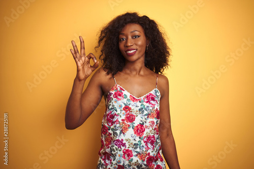 African american woman wearing floral summer t-shirt over isolated yellow background smiling positive doing ok sign with hand and fingers. Successful expression.