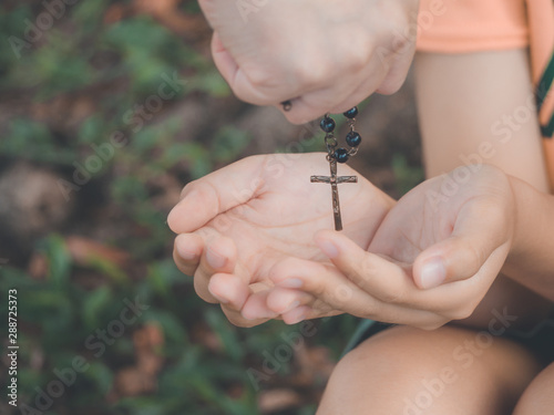 Religious young boy praying hands with the cross to God at park. 