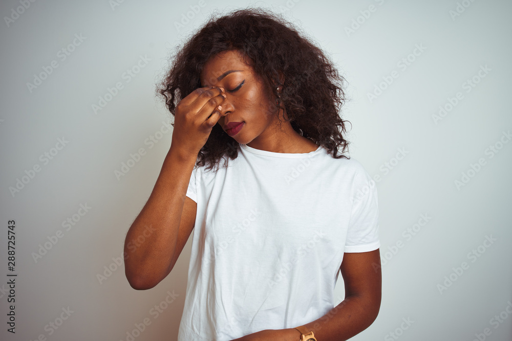 Young african american woman wearing t-shirt standing over isolated white background tired rubbing nose and eyes feeling fatigue and headache. Stress and frustration concept. Young african american woman wearing t-shirt standing over isolated white background tired rubbing nose and eyes feeling fatigue and headache. Stress and frustration concept.