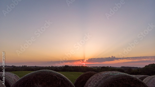 Sunrise over trees and round hay bales in a Nebraska field.