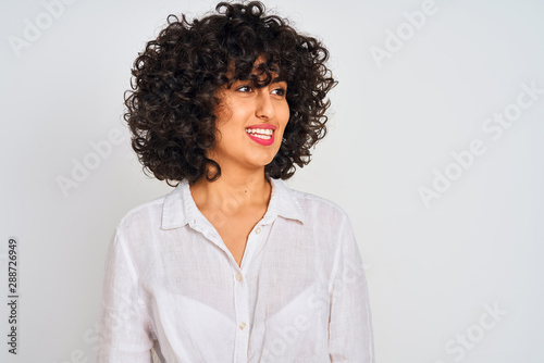 Young arab woman with curly hair wearing casual shirt over isolated white background looking away to side with smile on face, natural expression. Laughing confident.