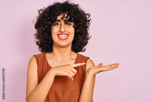 Young arab woman with curly hair wearing t-shirt over isolated pink background very happy pointing with hand and finger