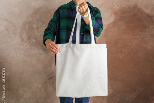 Young woman holding tote bag against brown background, empty space