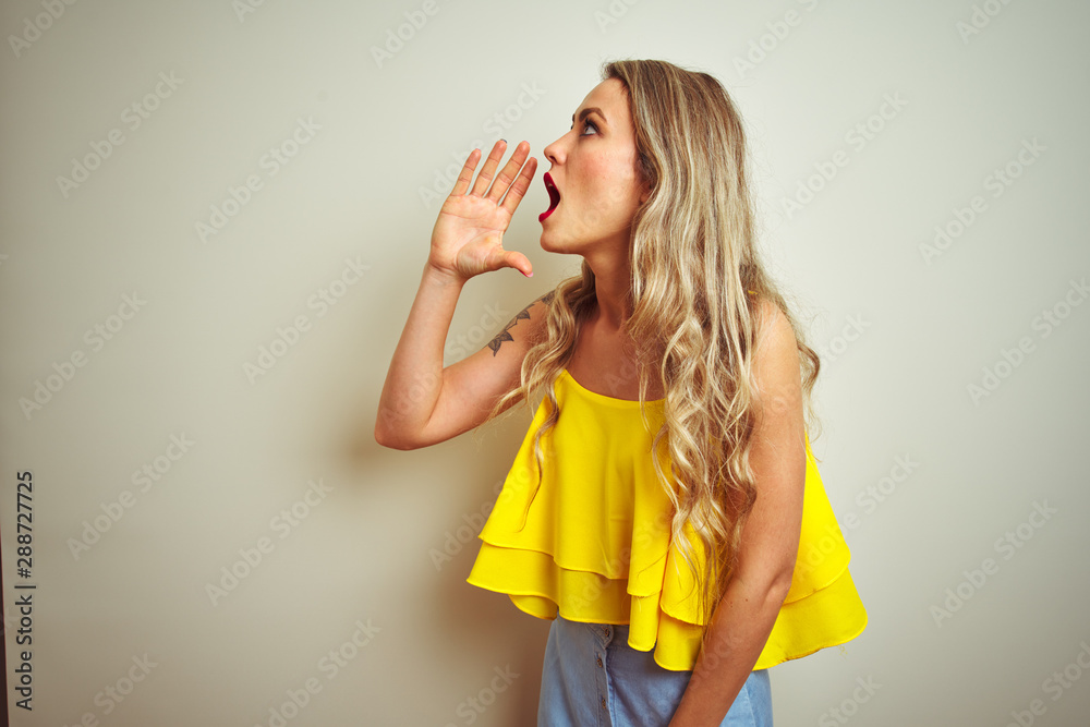 Young beautiful woman wearing yellow t-shirt standing over white isolated background shouting and screaming loud to side with hand on mouth. Communication concept. Young beautiful woman wearing yellow t-shirt standing over white isolated background shouting and screaming loud to side with hand on mouth. Communication concept.