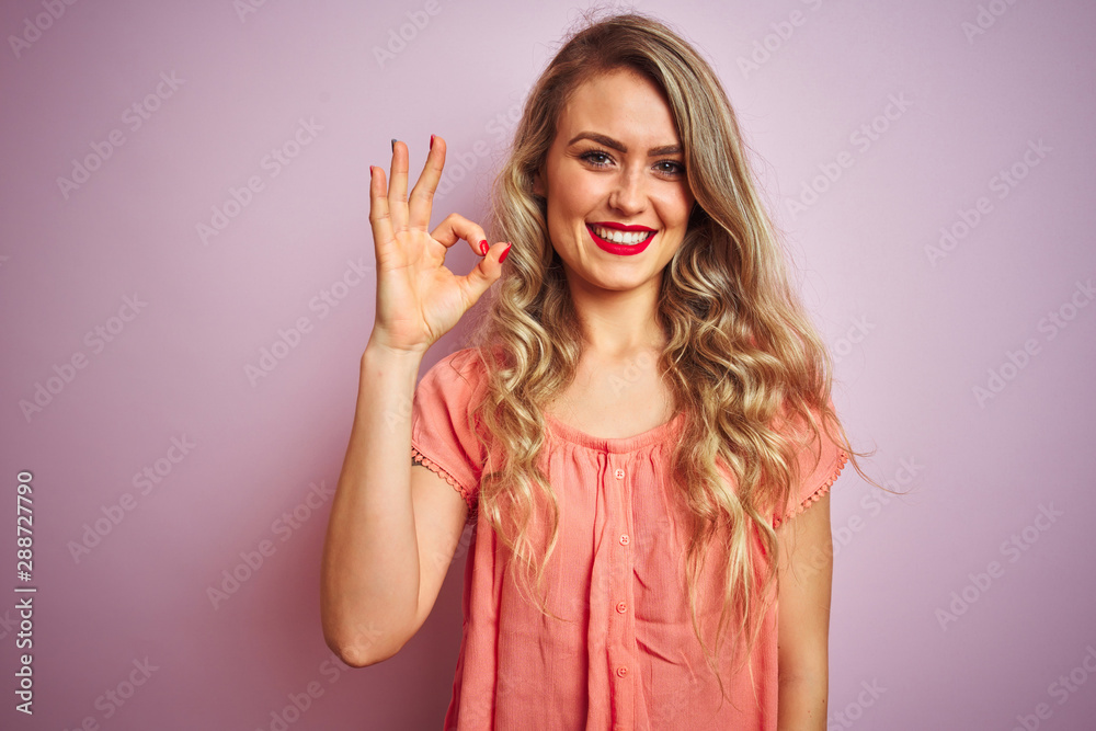 Young beautiful woman wearing t-shirt standing over pink isolated background smiling positive doing ok sign with hand and fingers. Successful expression. Young beautiful woman wearing t-shirt standing over pink isolated background smiling positive doing ok sign with hand and fingers. Successful expression.