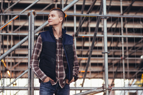 Cute young guy traveler posing against a background of barred building with iron structures. The concept of tourist walks around the city © Rithor