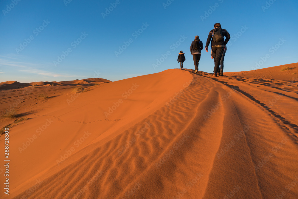 Three hikers are goiong up on the sand Dune in Erg Chebbi desert, Morocco