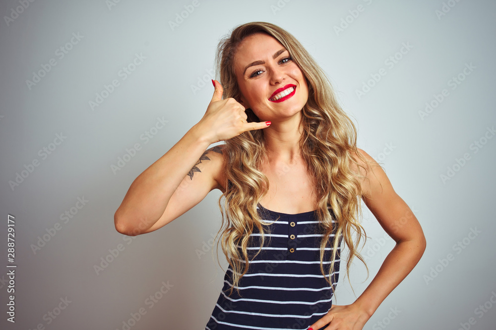 Young beautiful woman wearing stripes t-shirt standing over white isolated background smiling doing phone gesture with hand and fingers like talking on the telephone. Communicating concepts. Young beautiful woman wearing stripes t-shirt standing over white isolated background smiling doing phone gesture with hand and fingers like talking on the telephone. Communicating concepts.
