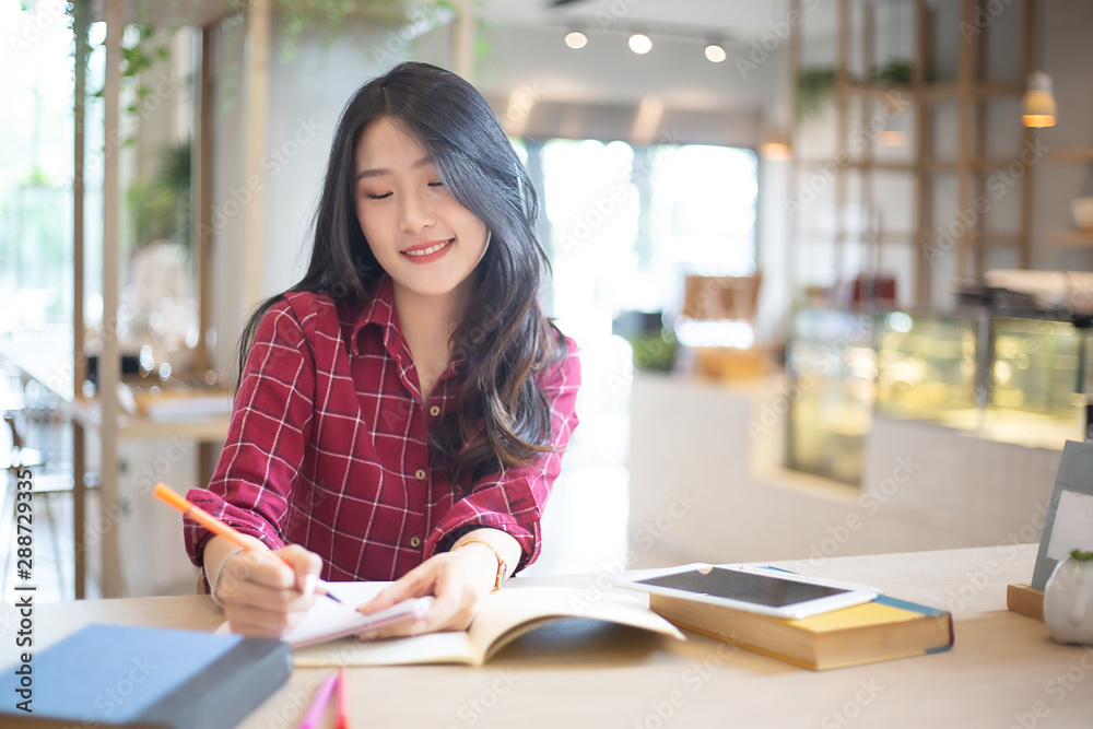 Young beautiful Asian woman reading a book while doing her homework in the modern co working space Young beautiful Asian woman reading a book while doing her homework in the modern co working space