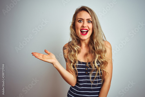 Young beautiful woman wearing stripes t-shirt standing over white isolated background pointing aside with hands open palms showing copy space, presenting advertisement smiling excited happy