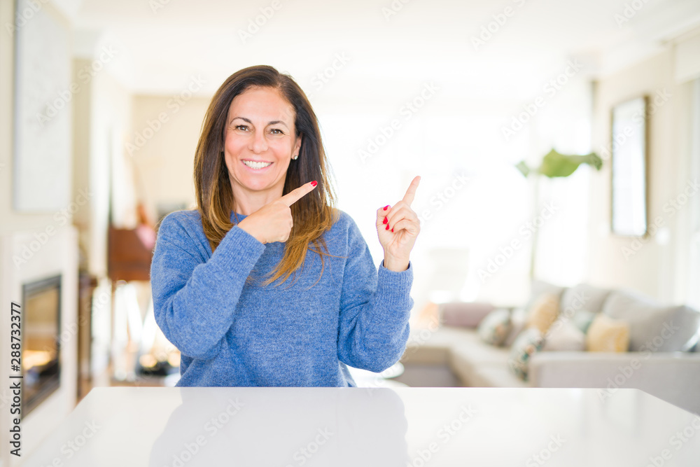 Beautiful middle age woman at home smiling and looking at the camera pointing with two hands and fingers to the side. Beautiful middle age woman at home smiling and looking at the camera pointing with two hands and fingers to the side.