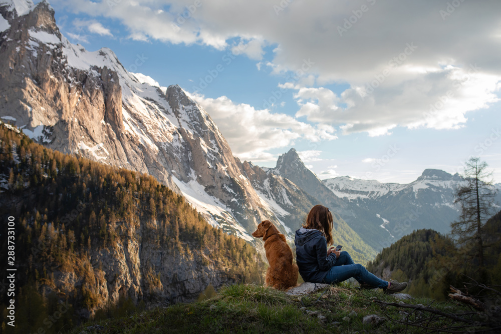 Fototapeta premium girl with a dog in the mountains. Autumn mood. Traveling with a pet. Nova Scotia Duck Tolling Retriever