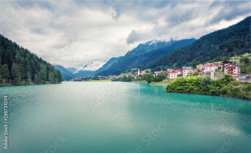 Gloomy summer view of Auronzo di Cadore and its lake in province of Belluno, Veneto, Italy. Dramatic morning scene of Dolomite Alps. Traveling concept background. Orton Effect.