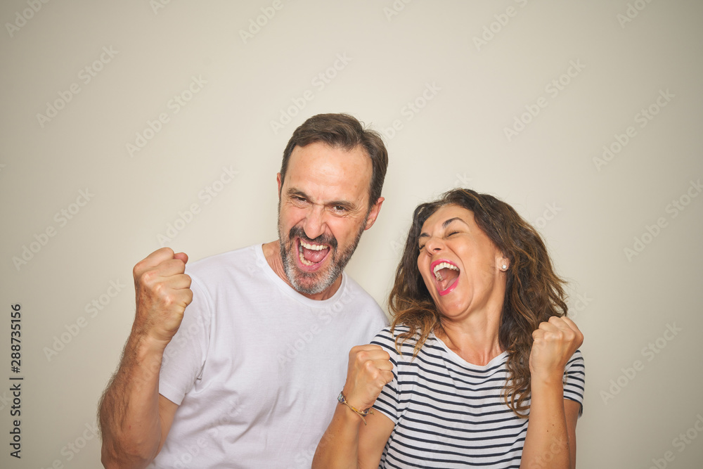 Beautiful middle age couple together standing over isolated white background very happy and excited doing winner gesture with arms raised, smiling and screaming for success. Celebration concept.