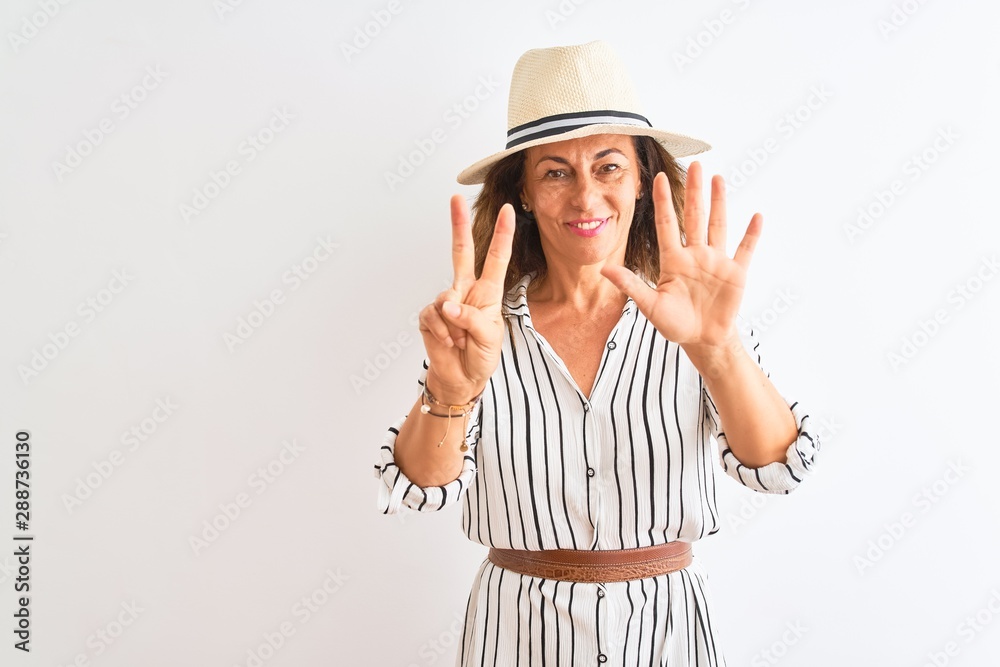 Middle age businesswoman wearing striped dress and hat over isolated white background showing and pointing up with fingers number seven while smiling confident and happy. Middle age businesswoman wearing striped dress and hat over isolated white background showing and pointing up with fingers number seven while smiling confident and happy.