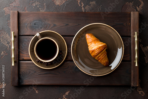 Cup of coffee with a croissant on a dark wooden tray