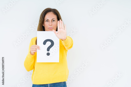 Middle age woman thinking and holding paper with question mark symbol over isolated background with open hand doing stop sign with serious and confident expression, defense gesture