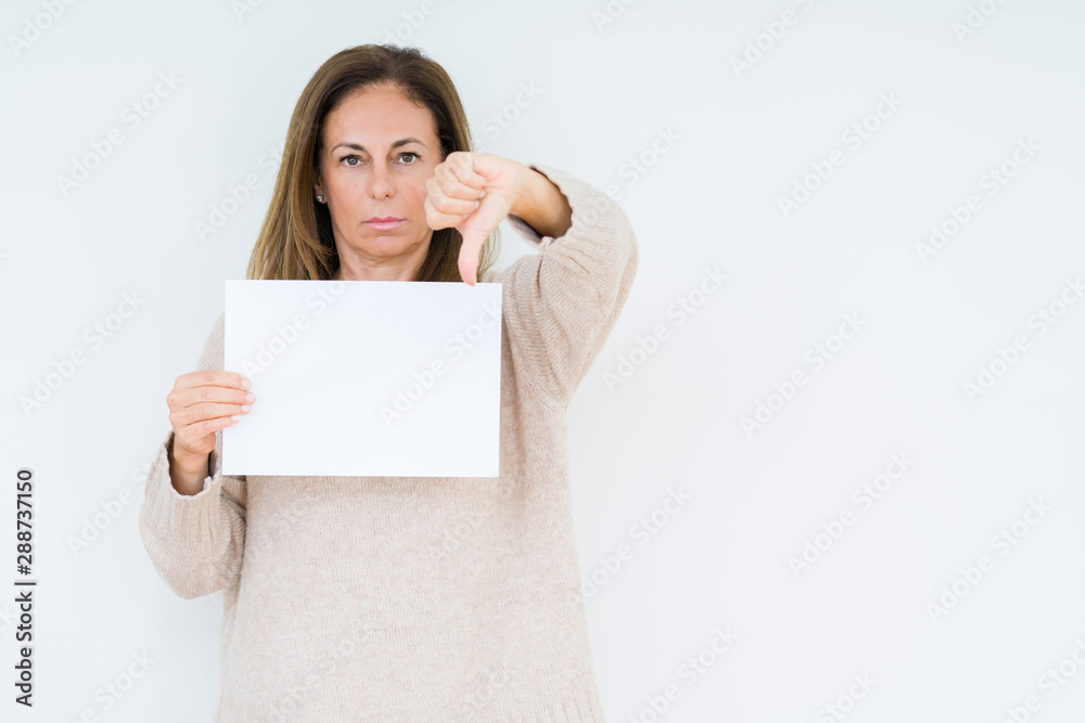 Middle age woman holding blank paper sheet over isolated background with angry face, negative sign showing dislike with thumbs down, rejection concept Middle age woman holding blank paper sheet over isolated background with angry face, negative sign showing dislike with thumbs down, rejection concept