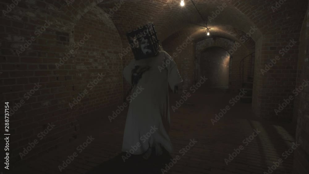 A funny ghost of a fat woman with a rusty cage on his head and with shackles on his hands dances in the gloomy corridor of old dungeon. A funny ghost of a fat woman with a rusty cage on his head and with shackles on his hands dances in the gloomy corridor of old dungeon.