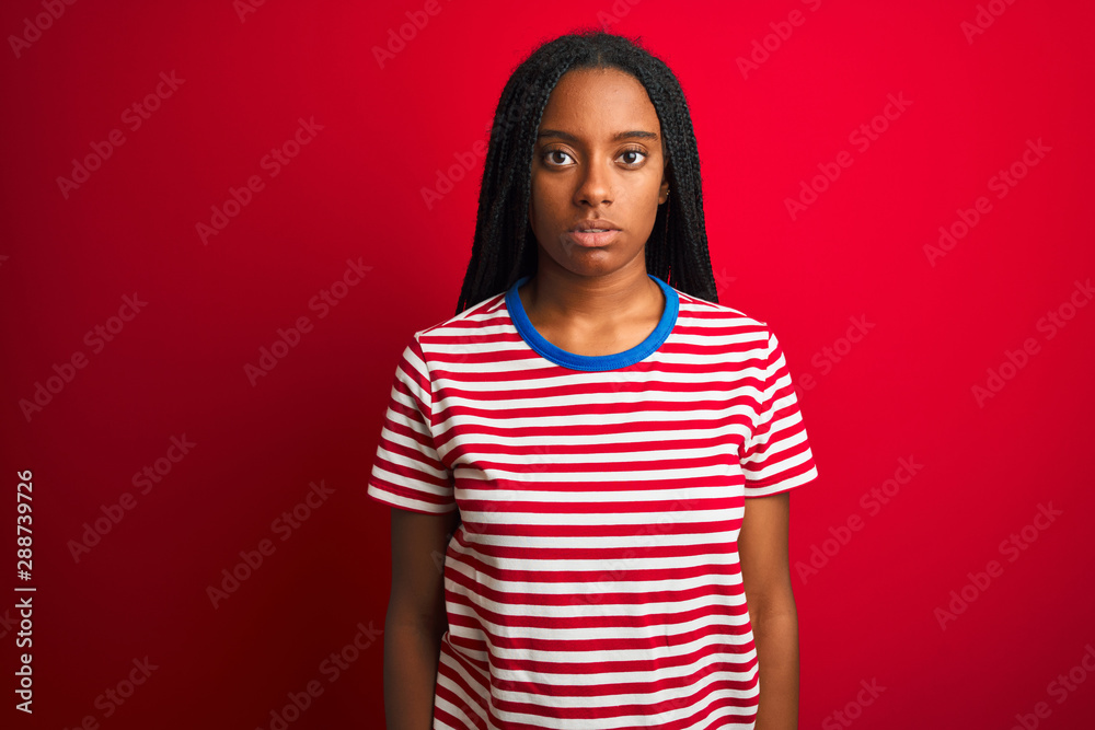 Young african american woman wearing striped t-shirt standing over isolated red background Relaxed with serious expression on face. Simple and natural looking at the camera. Young african american woman wearing striped t-shirt standing over isolated red background Relaxed with serious expression on face. Simple and natural looking at the camera.