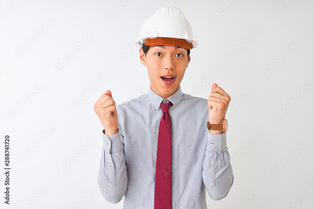 Chinese architect man wearing tie and helmet standing over isolated white background celebrating surprised and amazed for success with arms raised and open eyes. Winner concept. Chinese architect man wearing tie and helmet standing over isolated white background celebrating surprised and amazed for success with arms raised and open eyes. Winner concept.