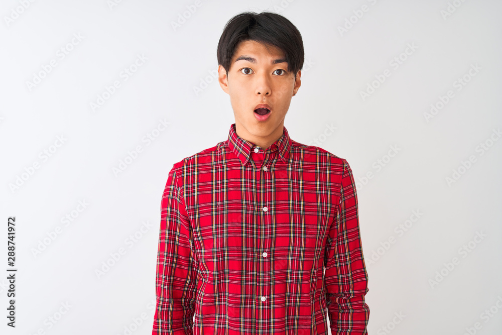 Young chinese man wearing casual red shirt standing over isolated white background afraid and shocked with surprise expression, fear and excited face. Young chinese man wearing casual red shirt standing over isolated white background afraid and shocked with surprise expression, fear and excited face.