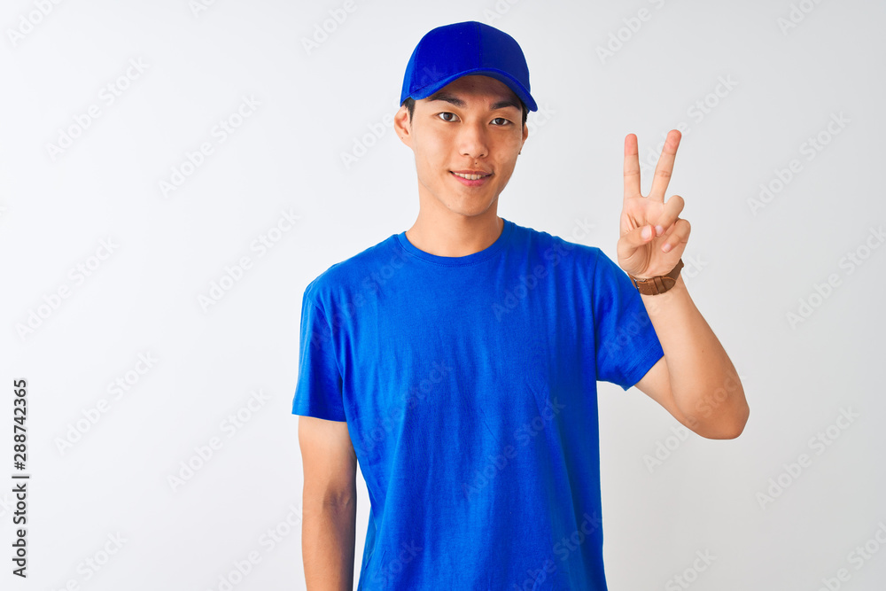Chinese deliveryman wearing blue t-shirt and cap standing over isolated white background showing and pointing up with fingers number two while smiling confident and happy.