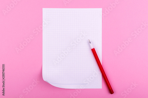 A white sheet of paper for drawings, texts, letters and notes, next to a red pen lies on a pink background